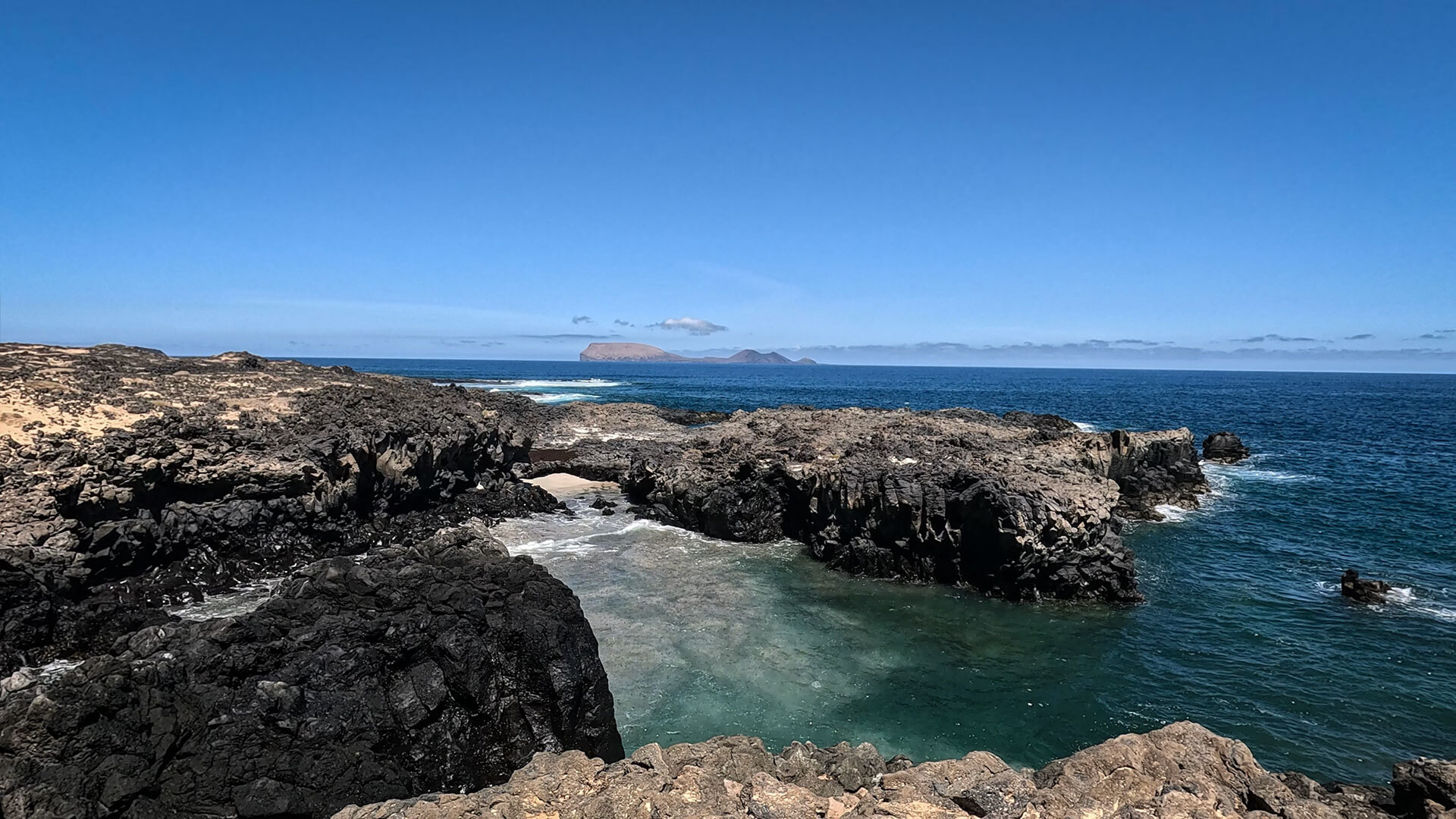 Felsbogen in einer Basaltbucht mit der Insel Alegranza im Hintergrund
